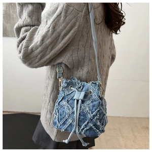 Detailed side view of blue denim bucket bag with diamond stitching and fringe tassels