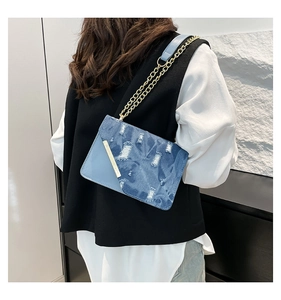 Detail of denim patchwork shoulder bag with golden chain and metallic bar accent