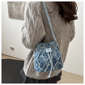 Rear view of model wearing a blue quilted denim bucket bag with frayed tassel details