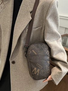 Brown monogram leather crossbody phone bag with wide fabric strap on a grey suit jacket