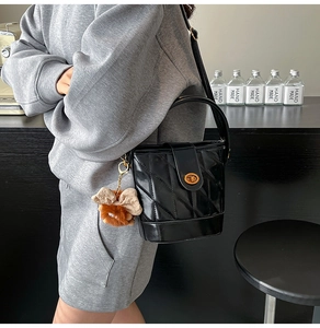 Detail of black quilted bucket bag with gold clasp and plush charm on a model