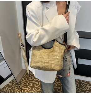 Detail of a beige woven straw shoulder bag with black leather trim worn by a model