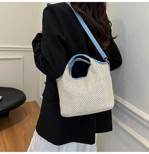 Detail of straw woven bucket bag with blue leather trim shown on shoulder