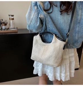 Detail of cream woven bucket bag with black leather handles and crossbody strap on a model