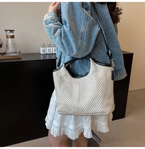 Detail of straw woven tote bag with black leather trim and crossbody strap on a model