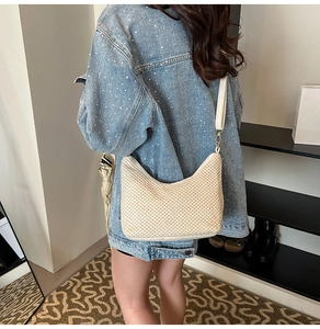 Detail of cream woven hobo bag with white leather strap and gold metal hardware