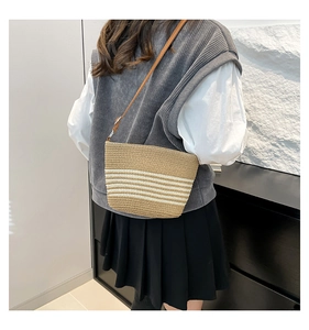 Detail of handwoven straw bucket bag with white stripes and brown leather strap