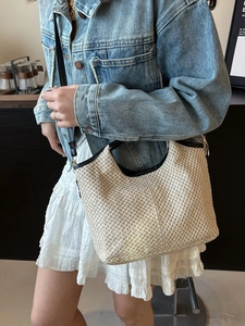 Beige woven bucket bag with black leather trim and crossbody strap for women