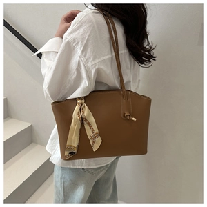 Brown leather tote bag detail with an elegant beige patterned scarf on the handle