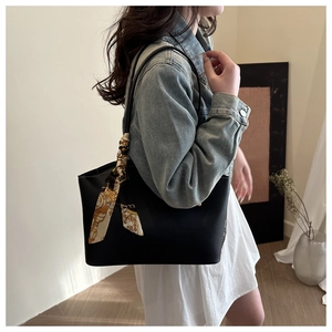 Detail of black tote bag with patterned silk scarf on strap, worn by a model
