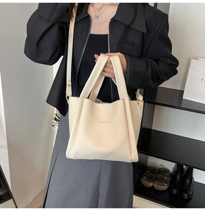 Detailed close-up of cream-colored pebble leather tote bag with debossed fashion text