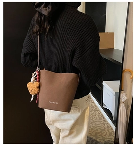 Braune matte Leder-Beuteltasche mit süßem Plüschbär-Anhänger und gewebten Riemendetails