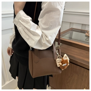 Brown lychee leather bucket bag with a cute plush monster charm shown on a shoulder