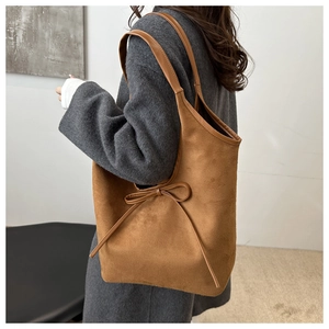 Brown matte suede tote bag with a bow accent shown as an elegant shoulder-carry detail