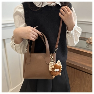 Detail of retro brown lychee grain leather bucket bag with a cute monster plush charm