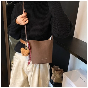 Detailansicht der dunkelbraunen matten Beuteltasche mit Bärenanhänger getragen am Model