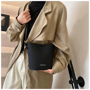 Detailansicht einer mattschwarzen Leder-Eimertasche kombiniert mit einem khakifarbenen Trenchcoat