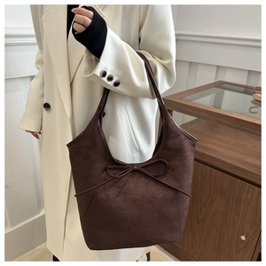 Detail of dark brown matte leather tote bag featuring a decorative bow on the front