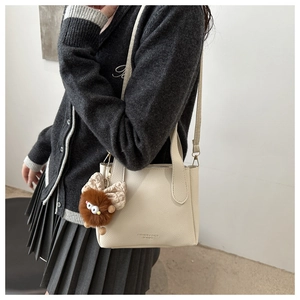 Detail of cream lychee leather bucket bag featuring fashion text and cute monster charm