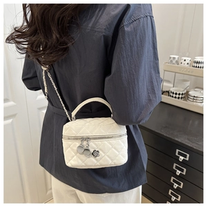 Détail du sac bandoulière matelassé blanc avec pendentif camélia et chaîne sur un modèle