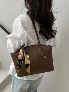 Minimalist dark brown leather tote bag with silk scarf on shoulder of a model