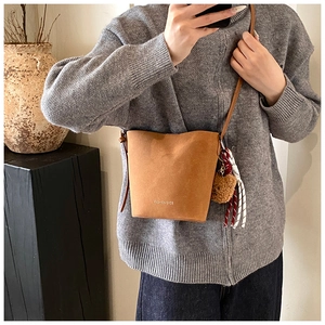 Braune matte Wildleder-Eimertasche mit Teddybären-Anhänger an einem Model getragen