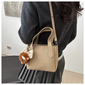 Detail of khaki lychee grain mini tote with cute monster charm and polka dot bow accessory