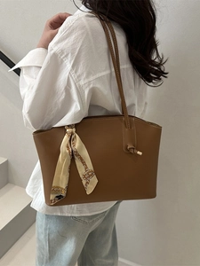 Brown leather tote bag with decorative silk scarf shown on model in minimalist interior