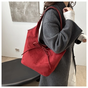 Détail du sac à bandoulière en daim rouge avec grand nœud décoratif et large bandoulière