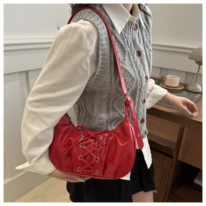 Detail of red crescent bag featuring silver eyelets and cross-lace design on leather