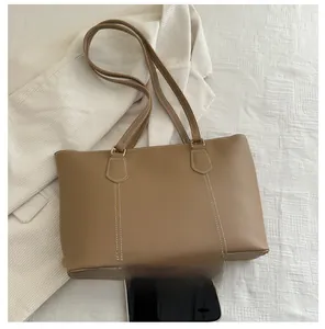 Detail view of khaki faux leather tote bag with white contrast stitching and gold rings