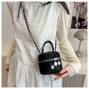 Detail of black quilted bucket bag with silver camellia charm and chain strap