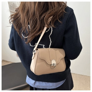 Detail of beige crossbody bag with silver oval metal lock worn over a blue sweater