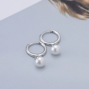 Minimalist silver hoop earrings with round white pearl pendants on blue background