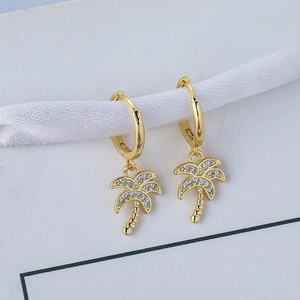 Close-up of 18K gold palm tree earrings with micro-set zircons on a white ribbon