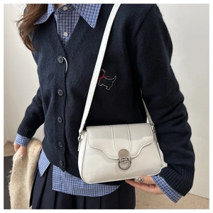 Close-up of white patent leather crossbody bag with silver buckle worn by a model
