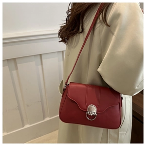 Detail of red leather crossbody bag with silver buckle worn over a beige trench coat