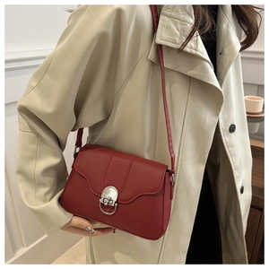 Detail of dark red crossbody baguette bag with silver buckle on beige trench coat