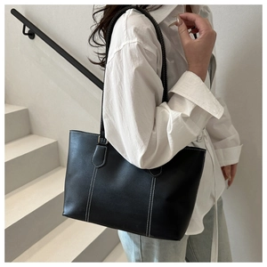 Detail of classic black leather tote bag featuring contrast white stitching and shoulder strap