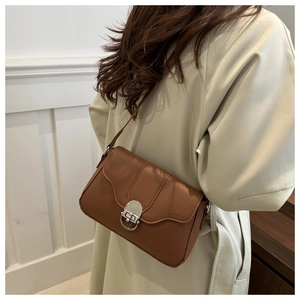 Detailed view of brown leather shoulder bag with vintage silver buckle on beige trench coat