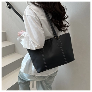 Detail shot of a black tote bag with white contrast stitching and long shoulder strap