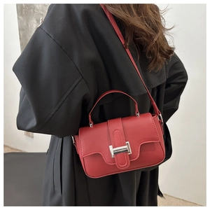Close-up of red matte leather flap bag with silver buckle worn on a black coat