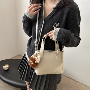 Minimalist beige lychee-patterned bucket bag with detachable strap and monster charm