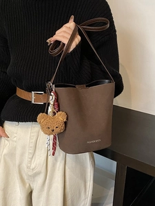 Braune matte Eimertasche aus Leder mit Plüschbär-Anhänger und schmalem Gurt