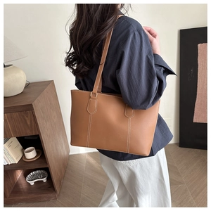 Detail of caramel leather tote bag with contrast stitching on a minimalist shoulder strap