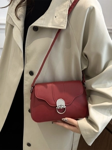 Deep red baguette shoulder bag with silver D-buckle shown on a model in a beige coat