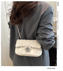 Rear view of a model wearing a quilted cream-white chain strap bag with a twist lock
