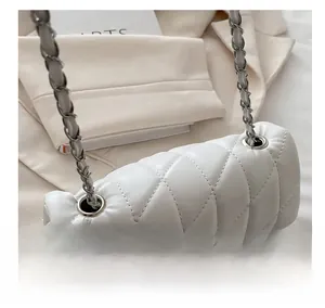 Close-up of white quilted faux leather texture with silver metal chain on handbag