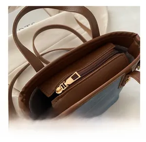Detailed top view of the smooth zipper closure on the blue denim and brown leather bucket bag