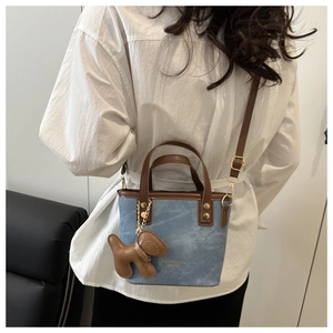 Detail of blue denim tote bag with brown leather trim worn by model in a natural setting